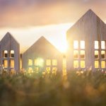 Three wooden house silhouettes against a sunset on grassy field.